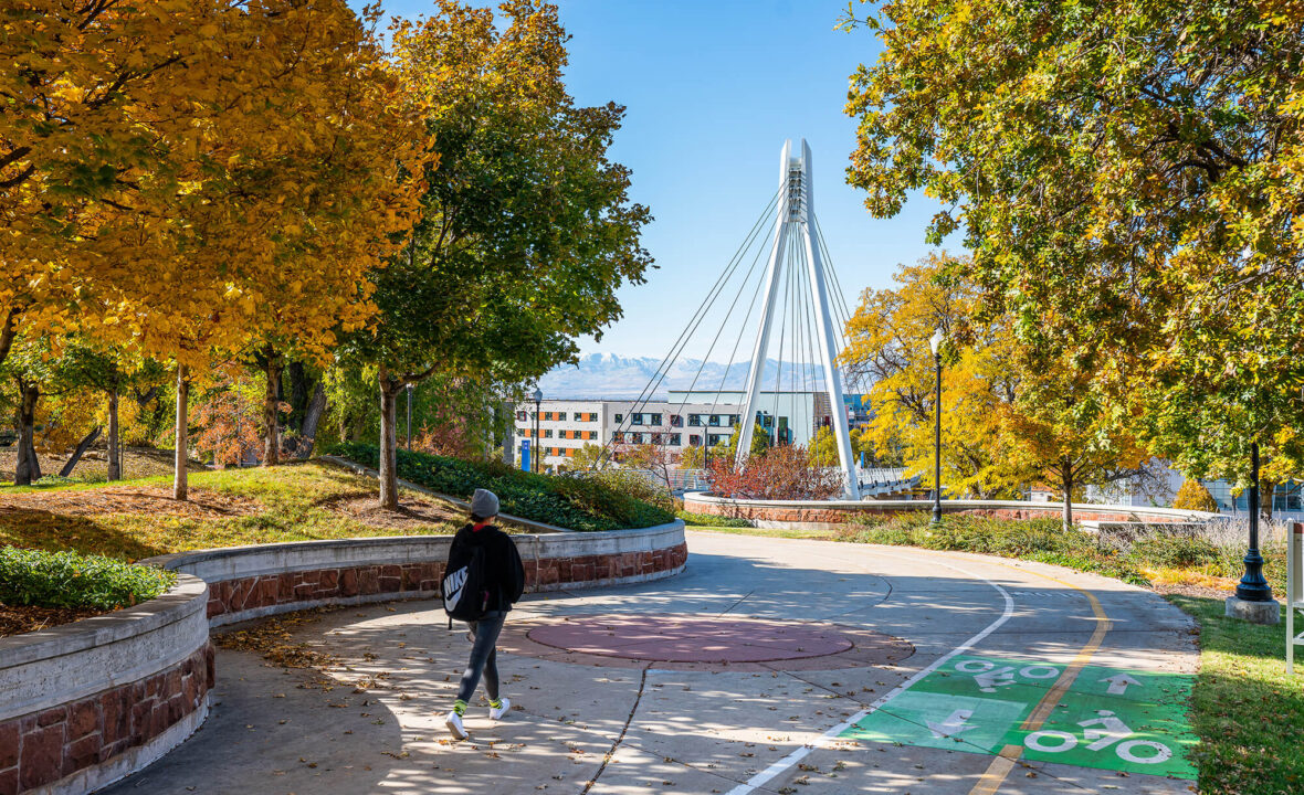 a student walks though campus in the fall, with the hospital and the suspension bridge in the background