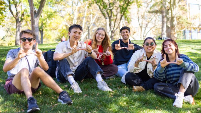 20241021-Ambassadors-Marketing-086-scaled-e1730999232285-768×433 a group of students on the grass making the U hand sign