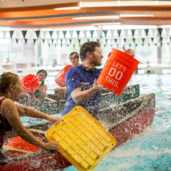 students in canoes splashing each other with buckets of water