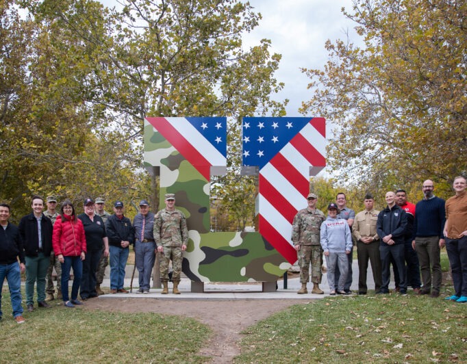 VeteransU-682×532 a large group poses around the block U, which has been wrapped with camo and USA flag colors