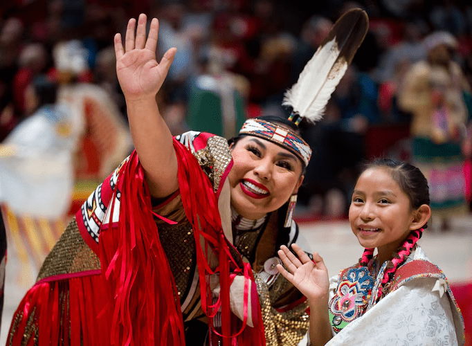 What-the-University-of-Utah-gives-the-Ute-Tribe-for-naming-rights-682×500 a couple of smiling Native American performers waving to an audience