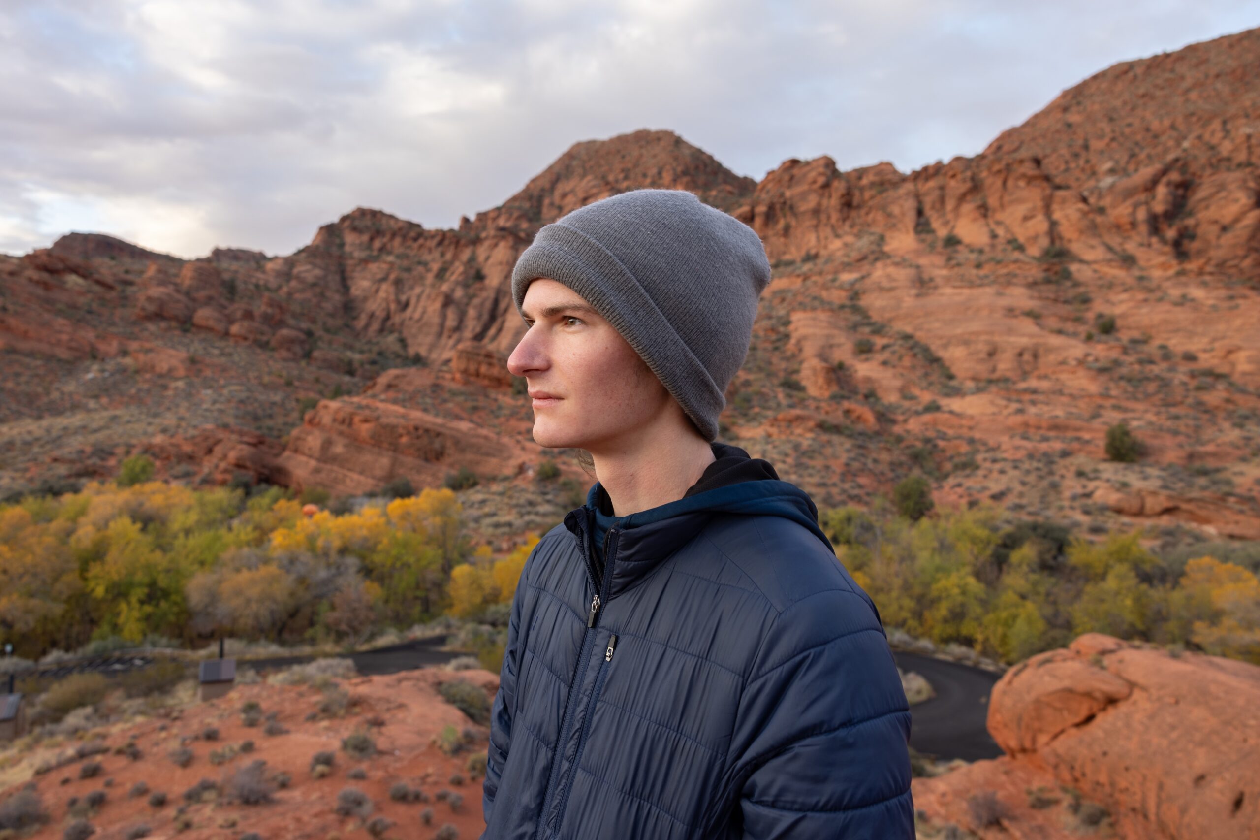 portrait of a student with a coat and beanie, looking off to the side with the red rocks of southern Utah behind them