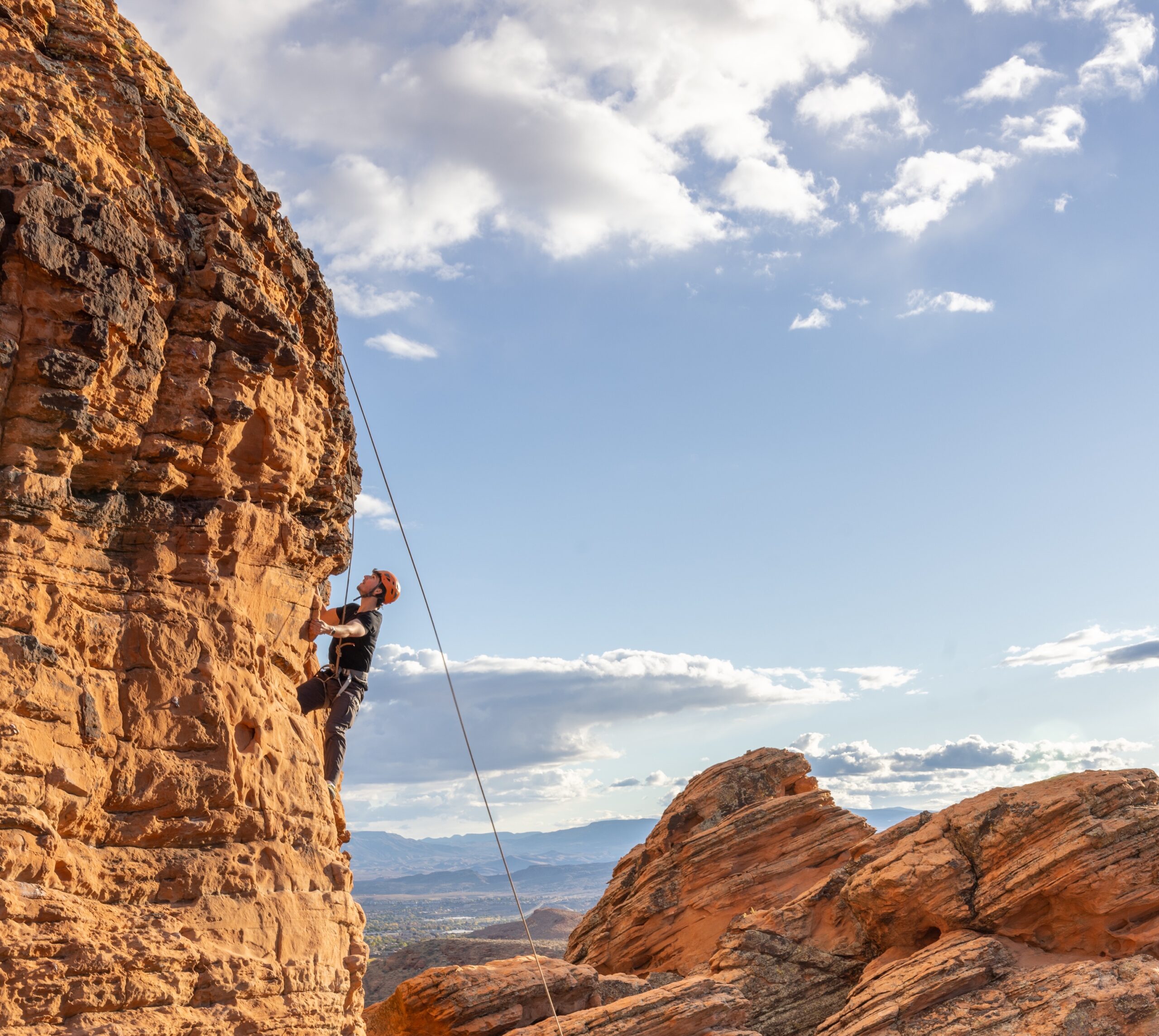 a student climbing a rock face with a wide open sky behind them